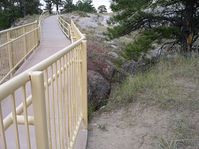 [Concrete walkway with a yellow-painted metal railing on both sides crosses the crevice in the land.]